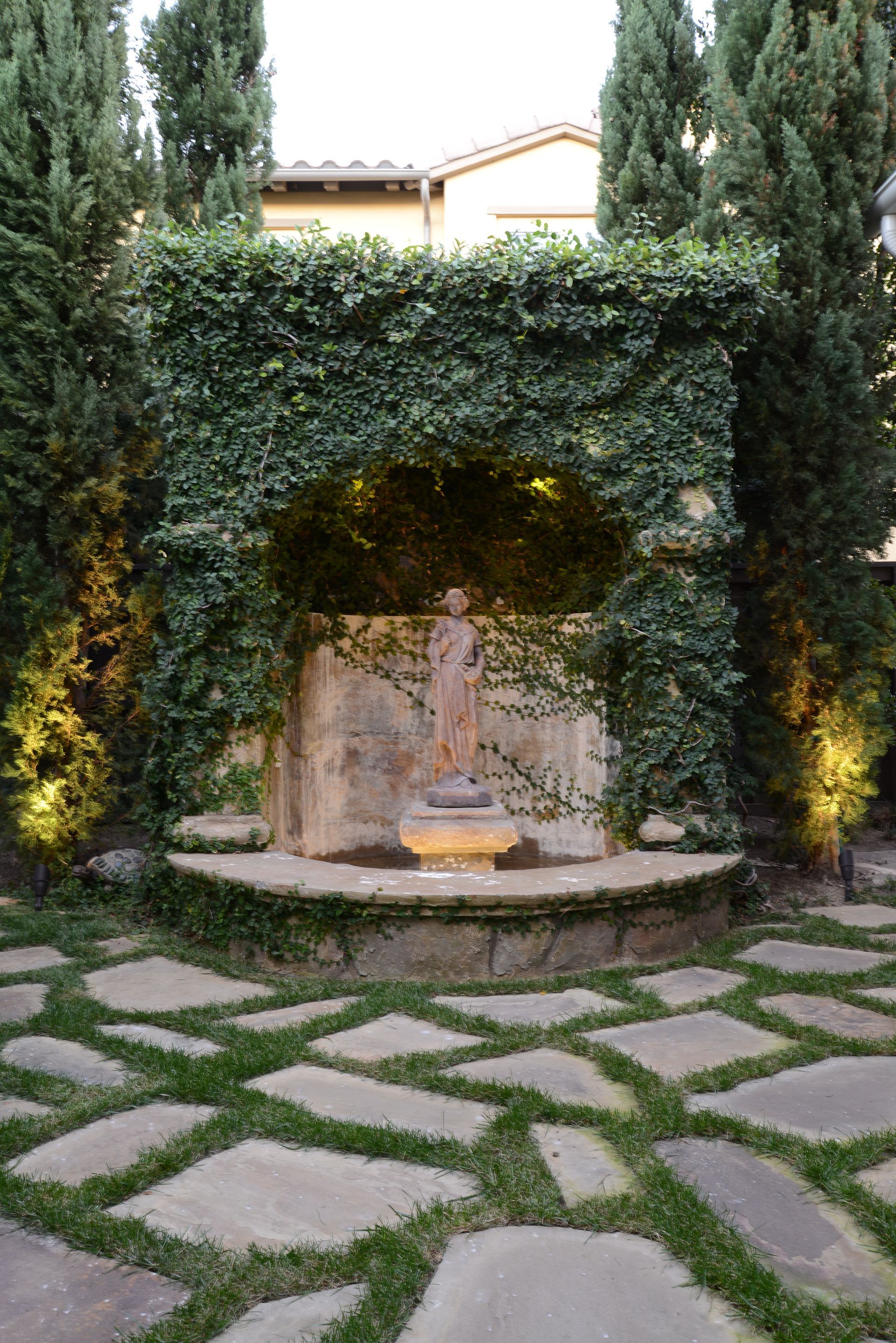 There is a fountain in the middle of the garden surrounded by trees.