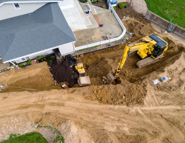 Aerial view of construction site with yellow excavator digging near a house.