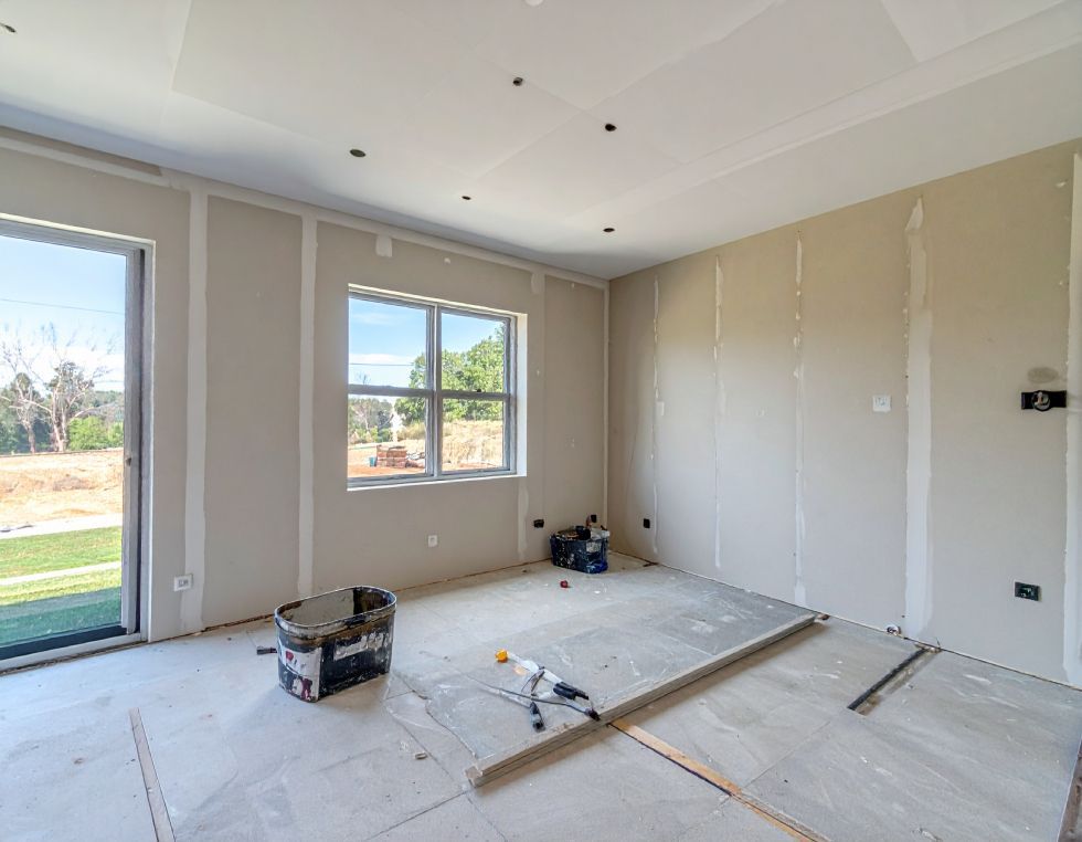 Interior of a room under construction with drywall on walls and ceiling, window and door.