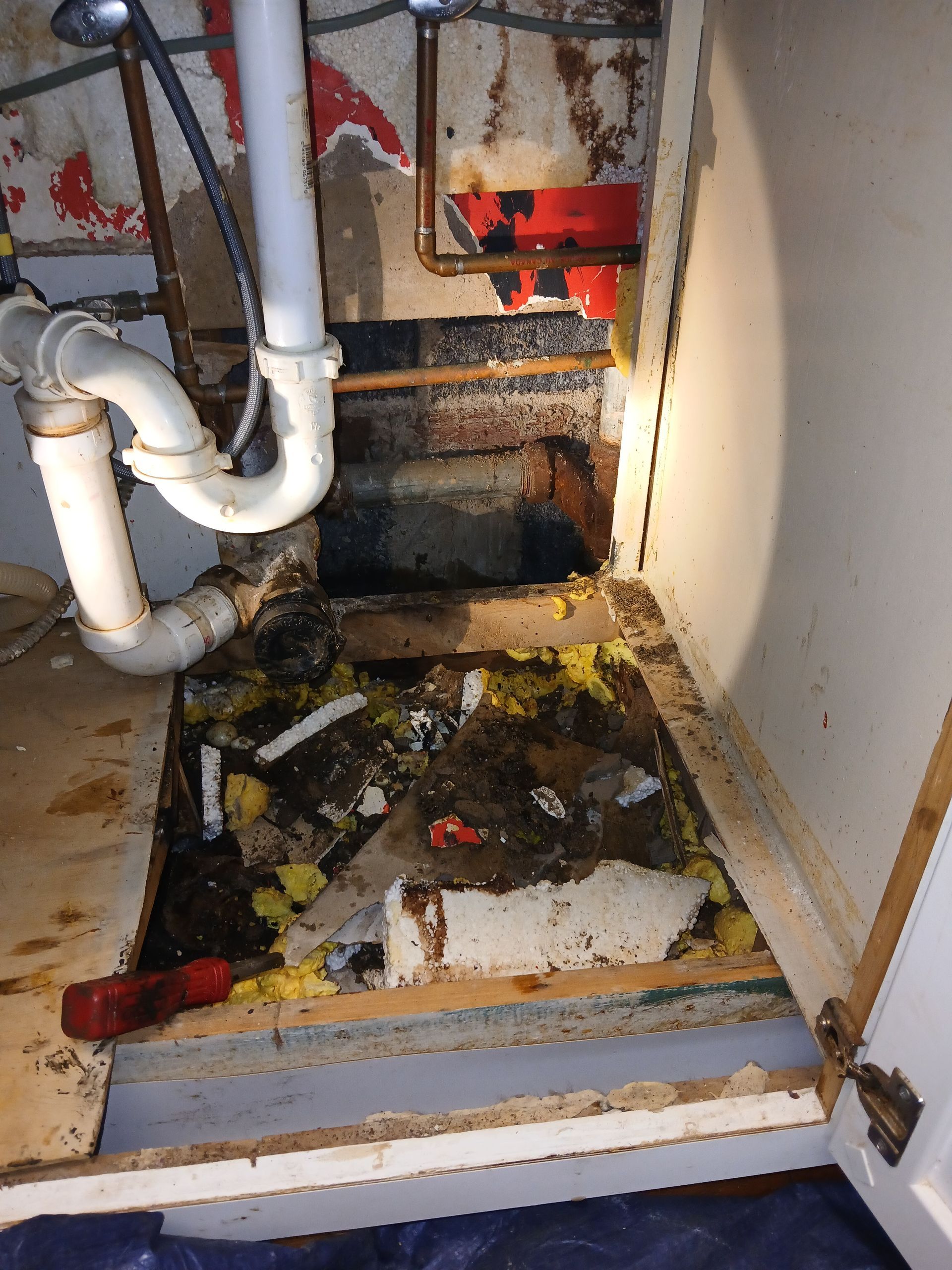 Debris-filled utility space under pipes with new exposed PVC piping.