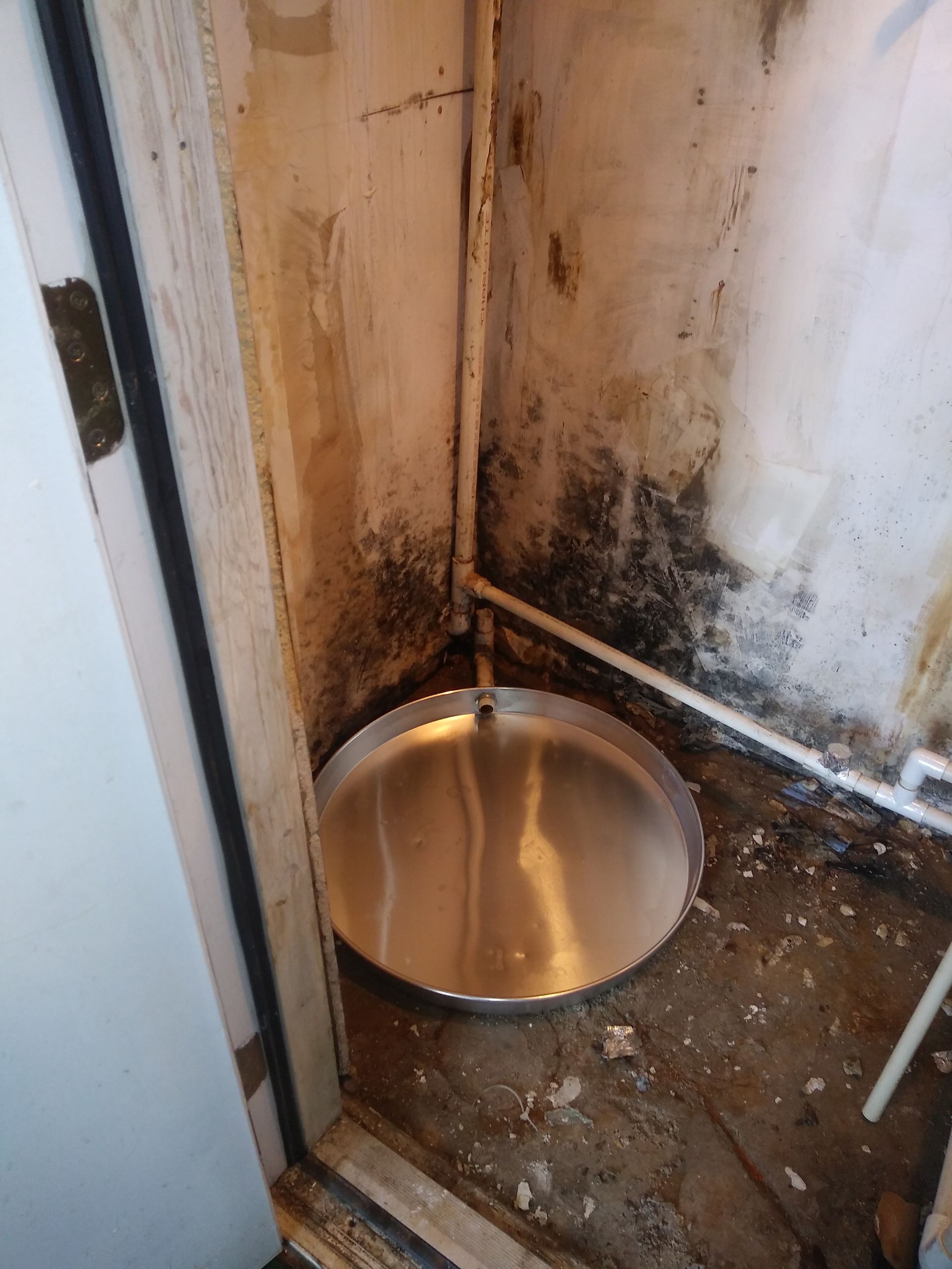 electric water heater base Corner of basement with a metal base for a new electric water heater on the floor near a doorway