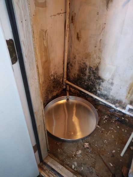 Corner of basement with a metal base for a new electric water heater on the floor near a doorway