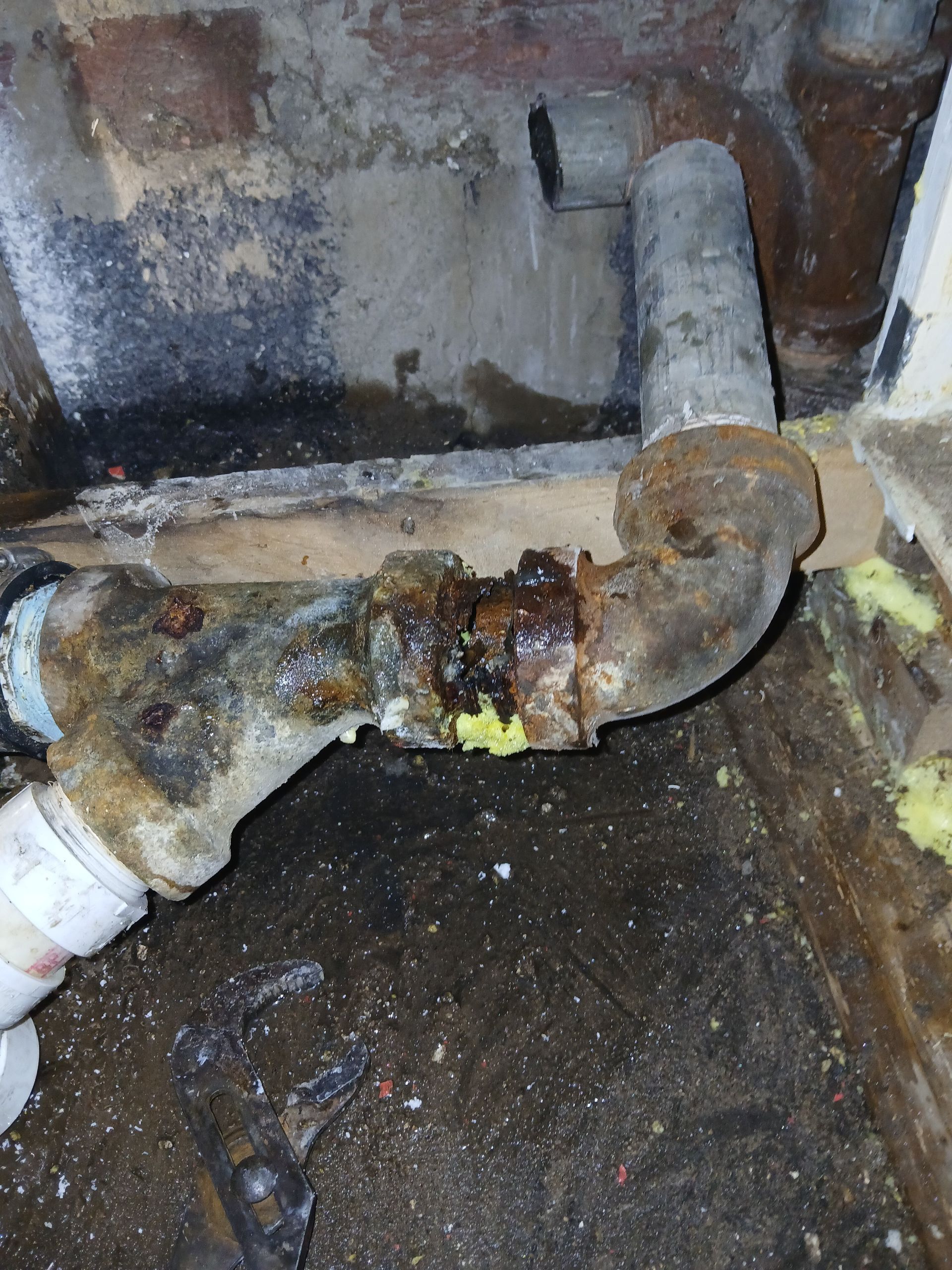 electric water heater base Rusty corroded plumbing pipes and fittings against a wall with water damage and debris on the floor