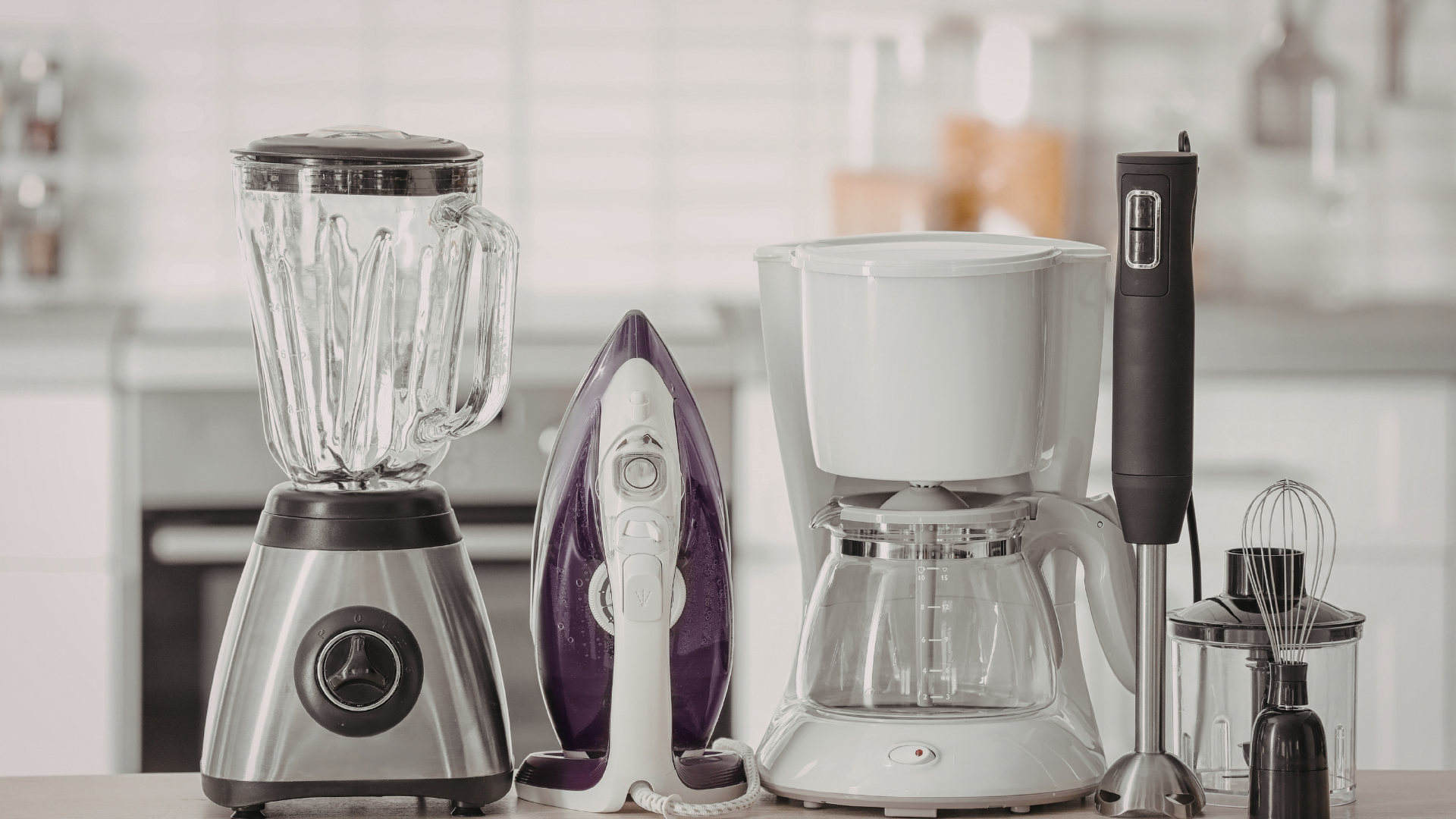 A countertop with a blender, a purple iron, a white coffee maker, and an immersion blender in a kitchen.