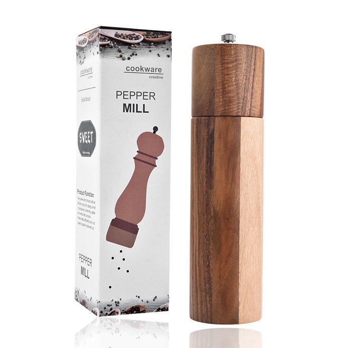 A wooden cylindrical pepper mill next to its white cardboard packaging.