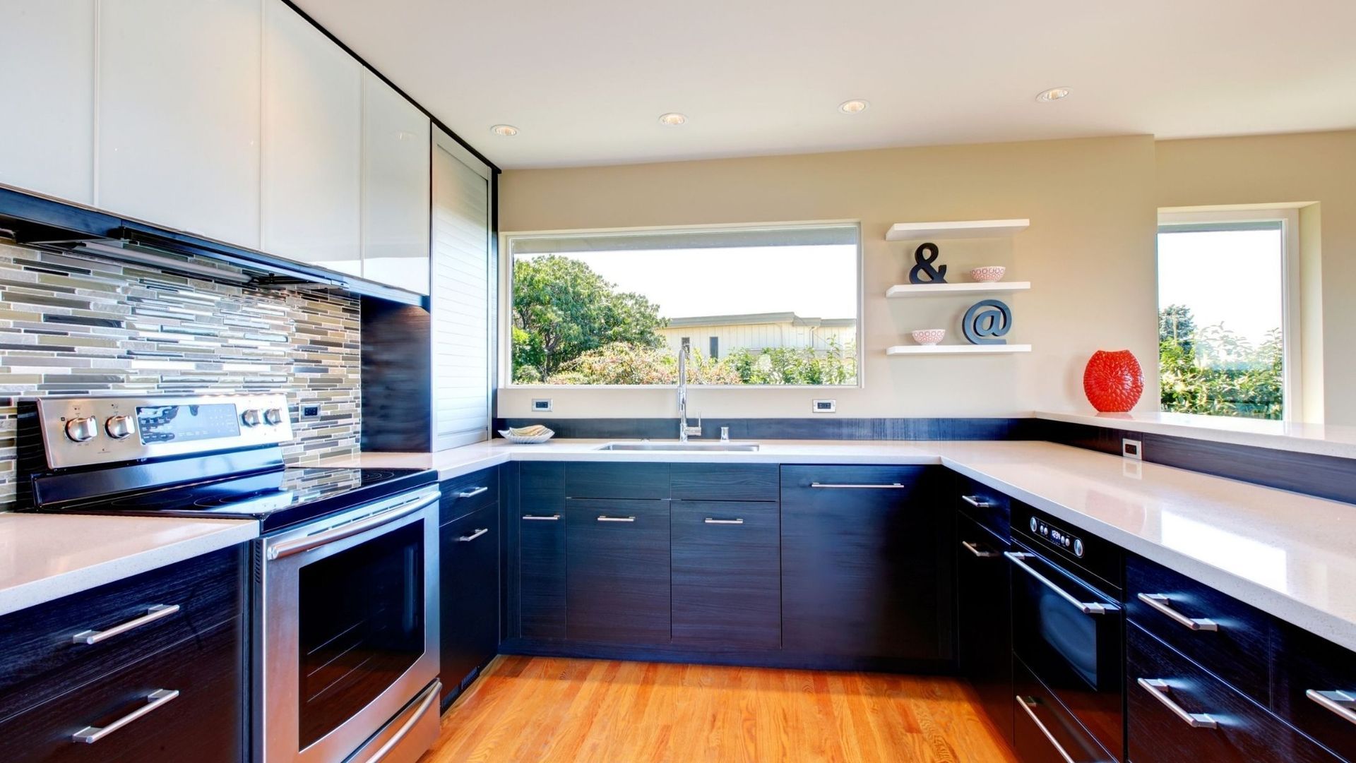 Modern kitchen with dark cabinets, stainless appliances, white counters, and wood flooring