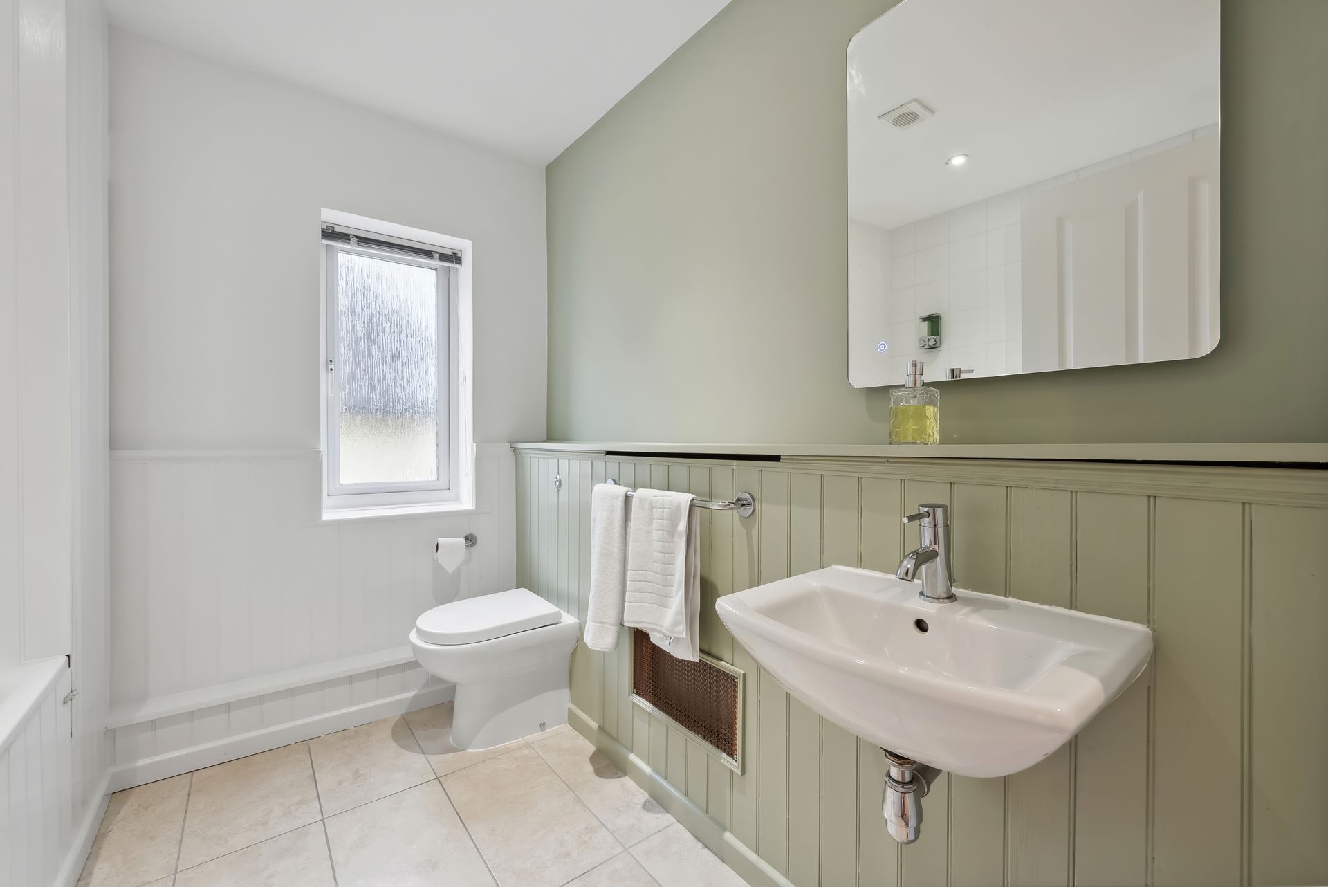 Bathroom with white fixtures, pale green walls, and a small window.