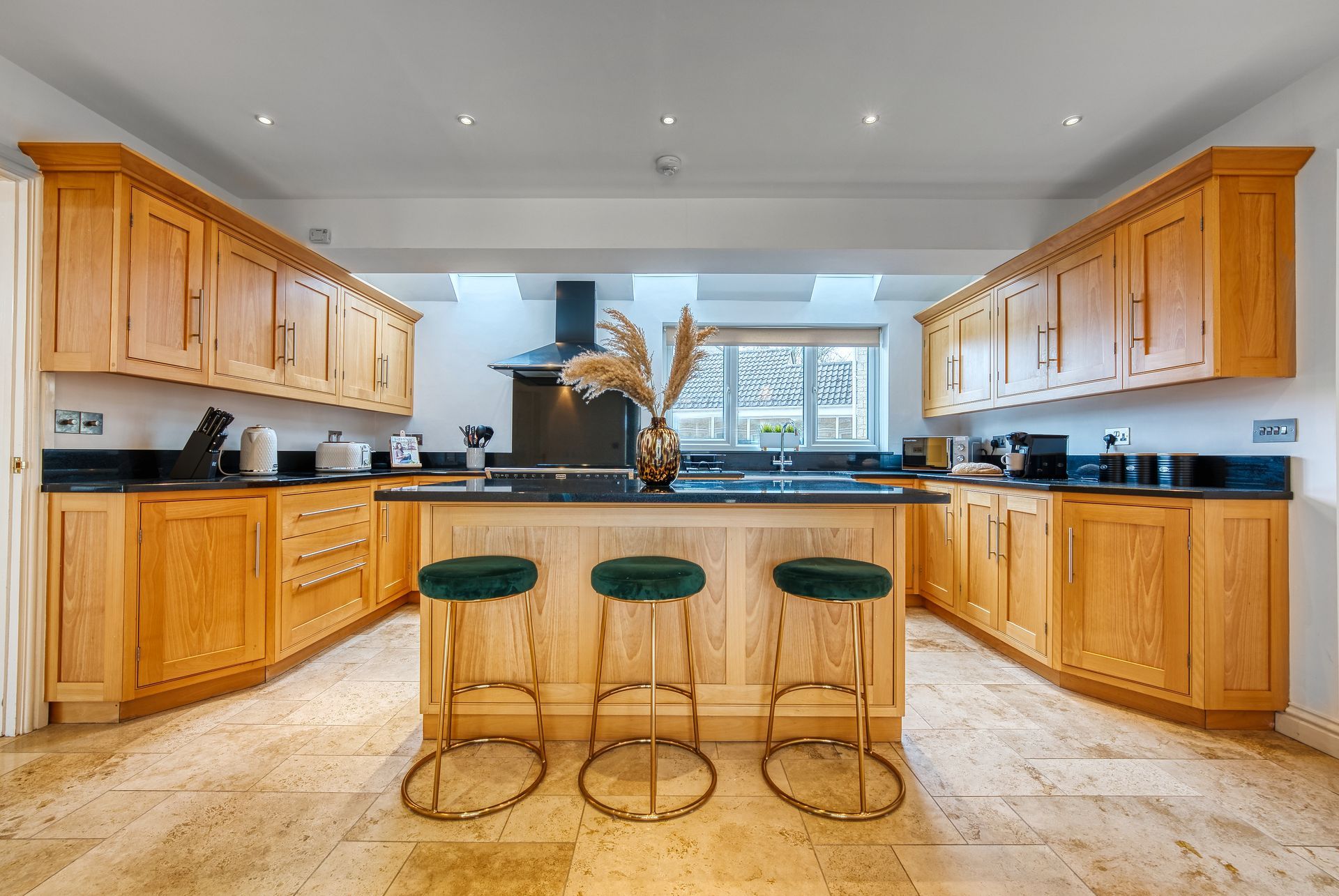 Kitchen with light wood cabinets, black countertops, and a central island with green stools.