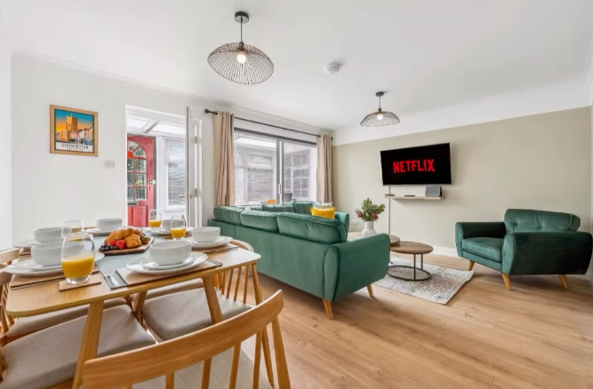 Living room with green sofa, TV, dining table set for four, and open doorway.