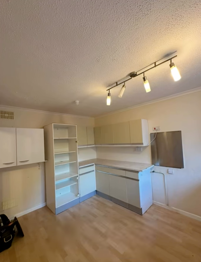 Empty kitchen with white cabinetry, open shelving, and light wood flooring. A track light illuminates the space.