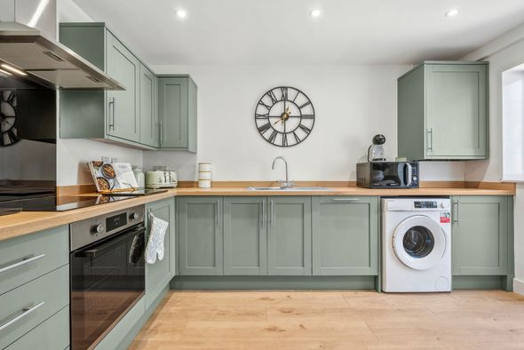 Green kitchen with wooden countertops, white appliances, and a clock on the wall.