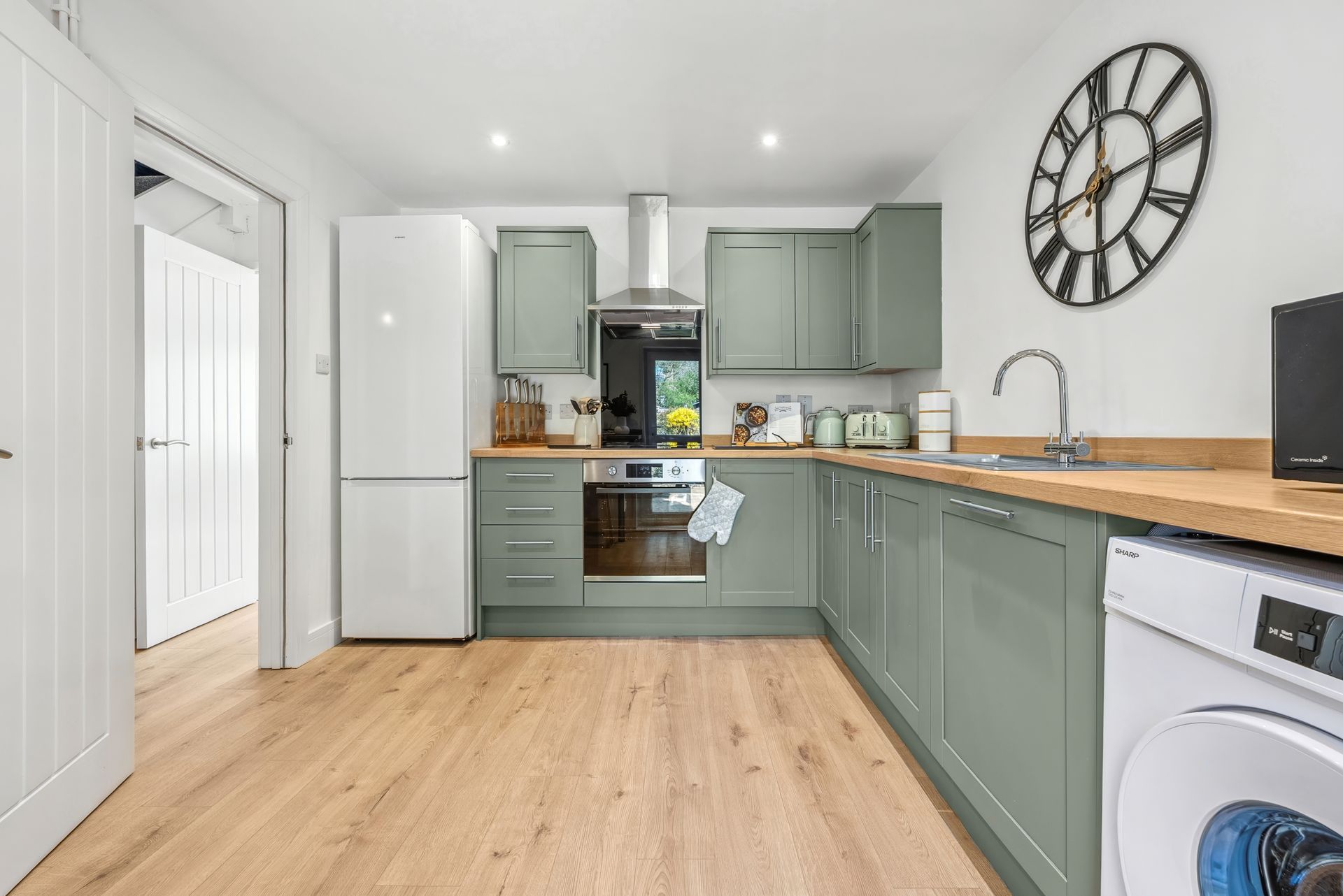 Kitchen with light green cabinets, wood countertop, stainless steel appliances, and large clock.