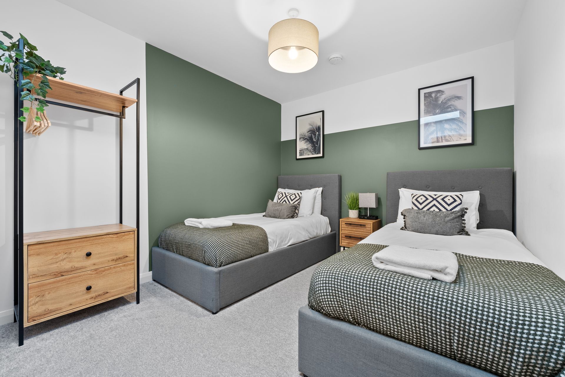 Two twin beds in a modern bedroom with green accent wall, wooden dresser, and artwork.