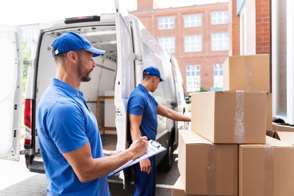 Two Delivery Men Are Loading Boxes Into A Van — Ahern's Removals In Taree, NSW