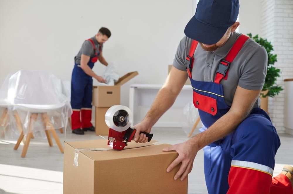 A Man Is Taping A Cardboard Box In A Living Room — Ahern's Removals In Laurieton, NSW