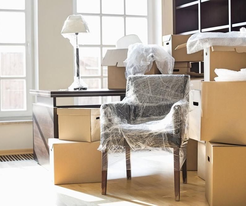 A Chair Wrapped In Plastic Is Sitting In A Room Surrounded By Cardboard Boxes — Ahern's Removals In Port Macquarie, NSW