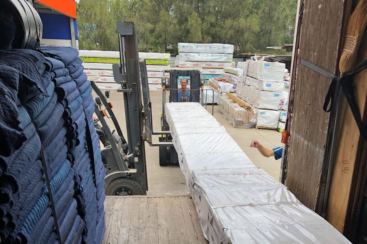 A Forklift Is Loading A Long Piece Of Wood Into A Truck — Ahern's Removals In Coffs Harbour, NSW