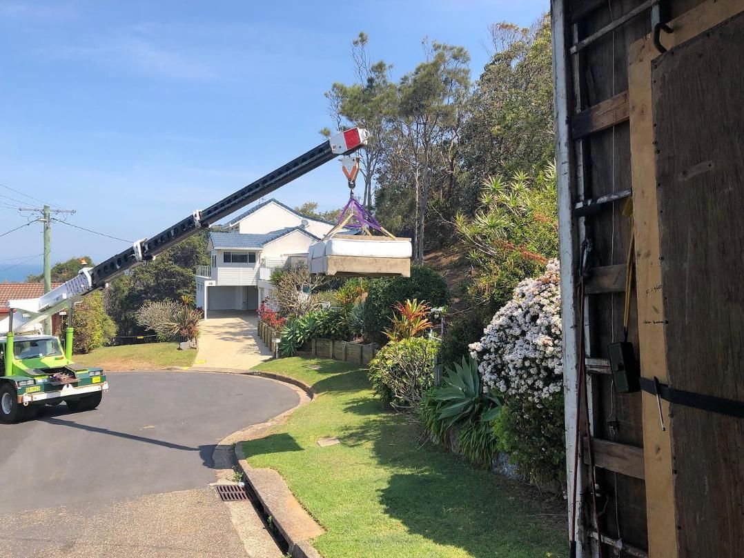 A Crane Is Lifting A Large Piece Of Wood Into A House — Ahern's Removals In Kempsey, NSW