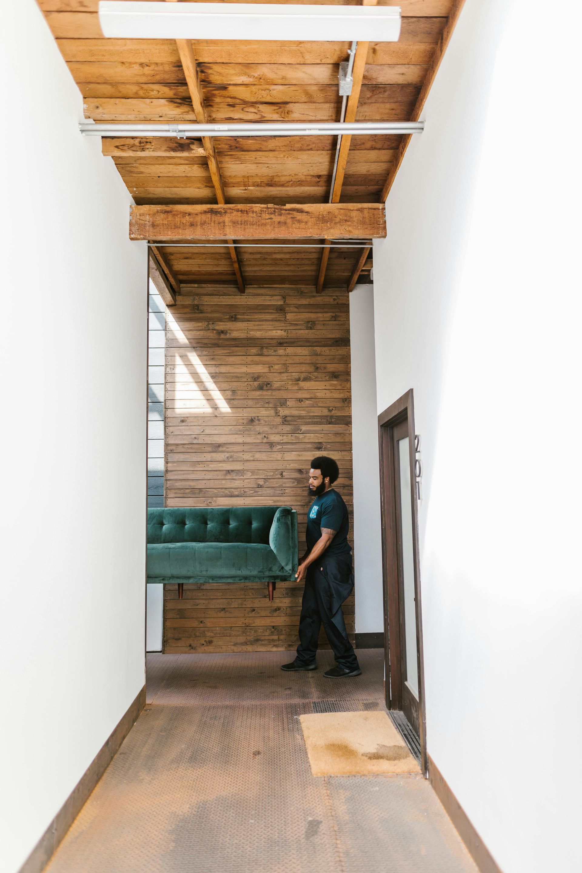 A Man Is Carrying A Green Couch Down A Hallway — Ahern's Removals In Canberra, ACT
