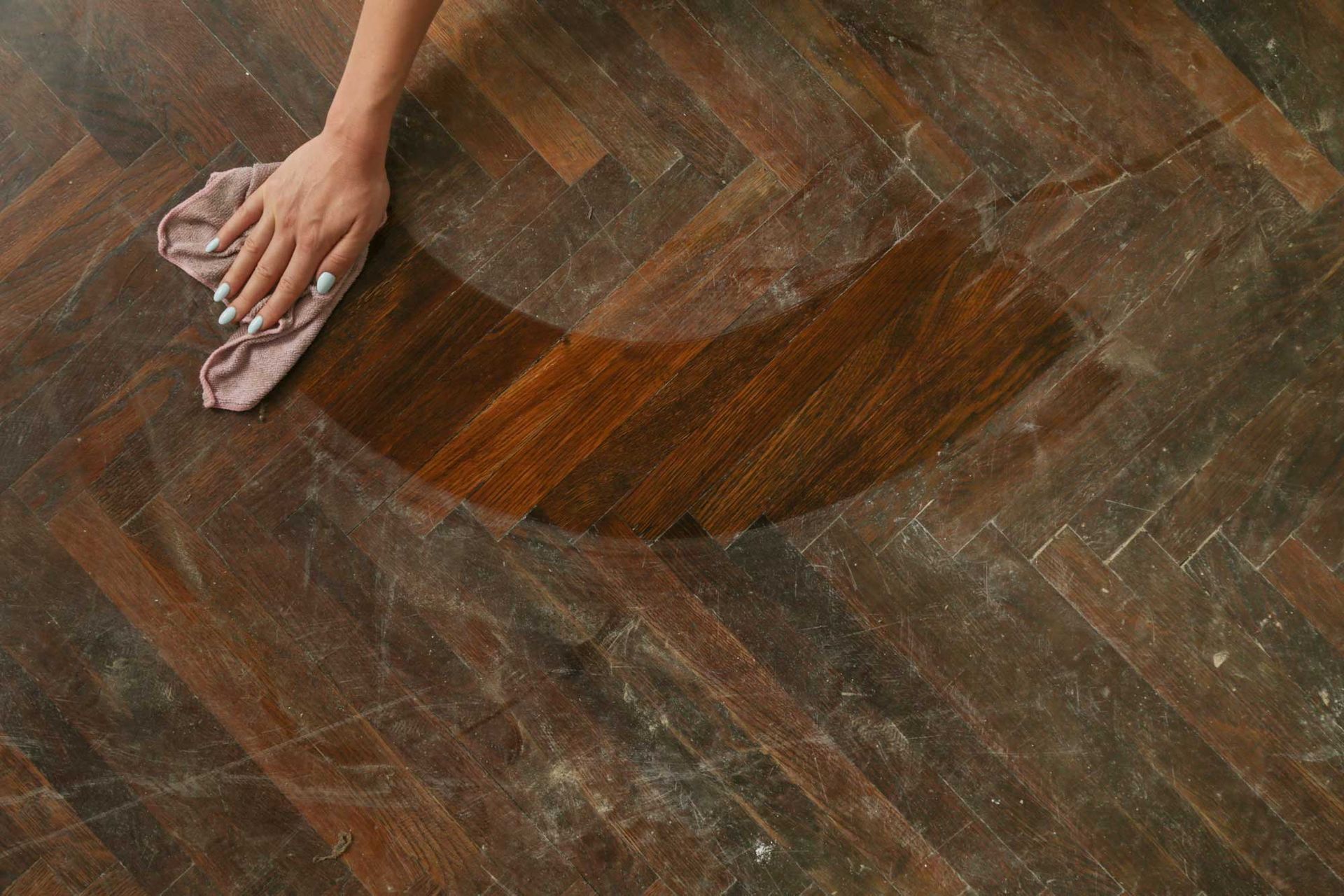 A woman's hand cleaning the wooden floor with a cloth.