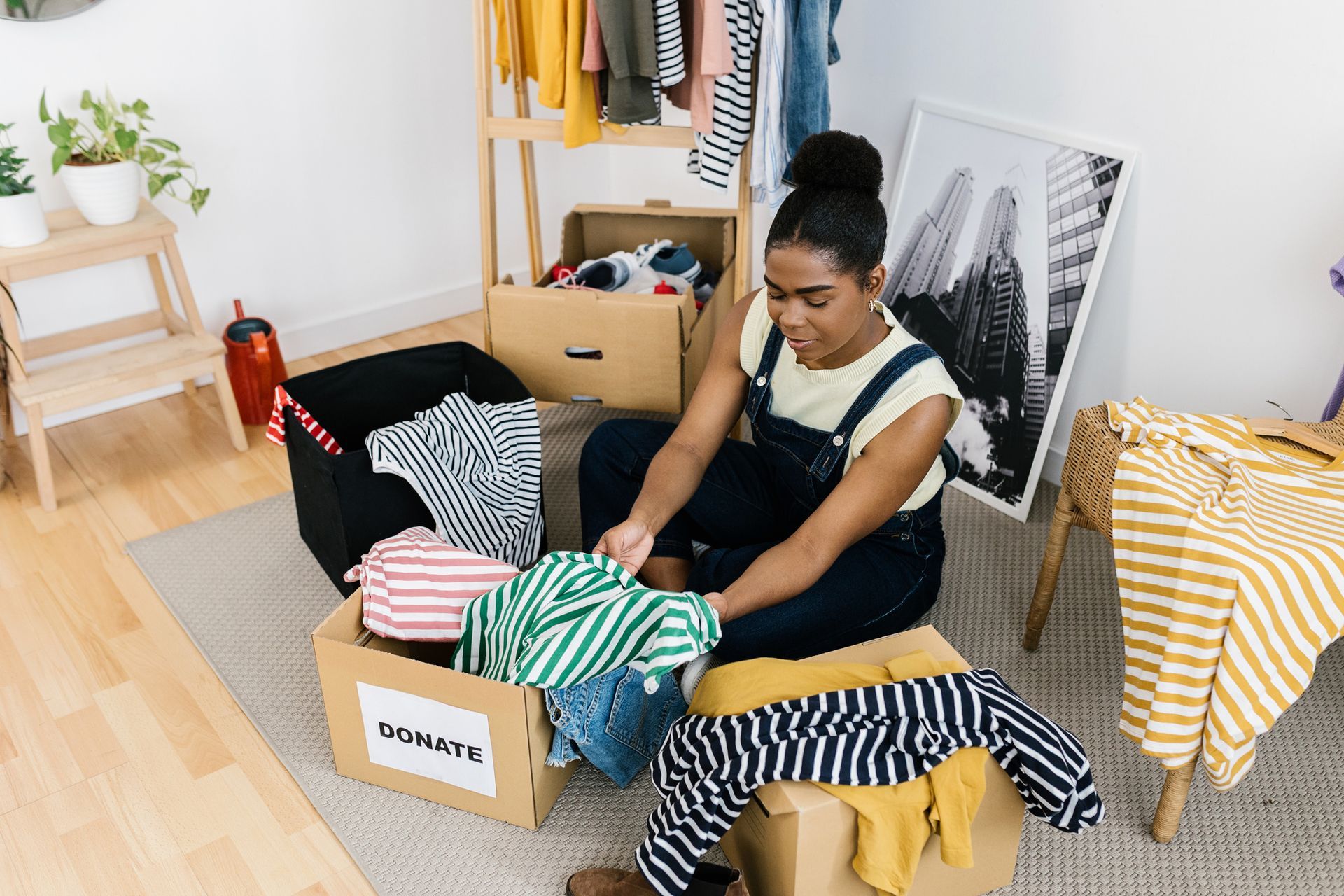 Woman sorting clothes into boxes in a well-lit room, possibly for donation.