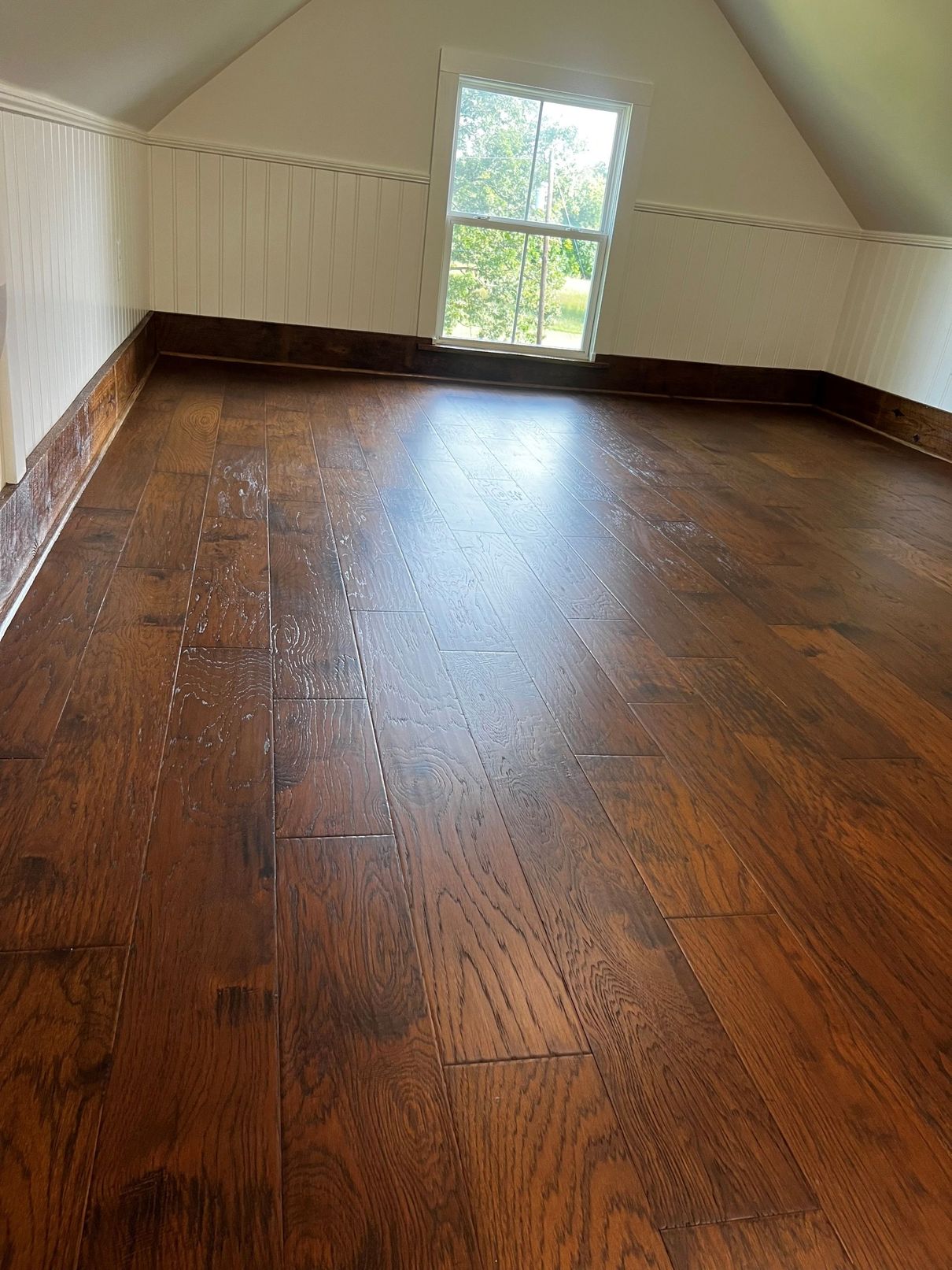 Dark wood floor in an attic room with a window and white walls.