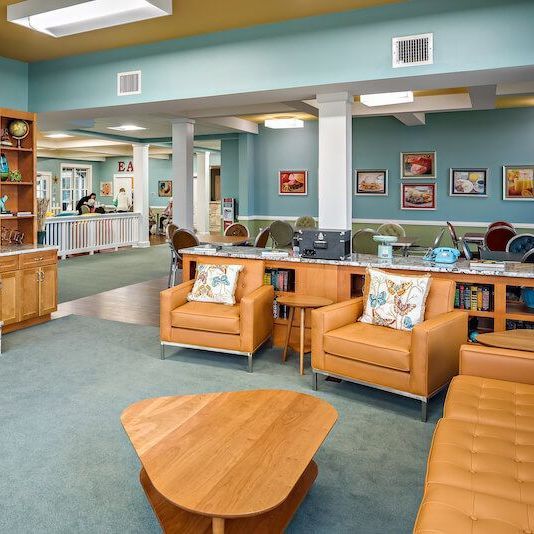 A cozy, inviting lounge area with leather furniture, bookshelves, and colorful artwork; blue-green walls.