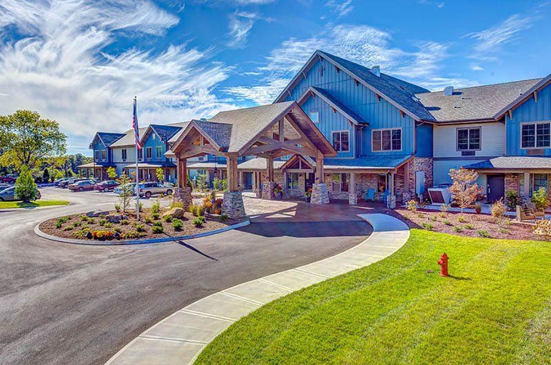 Large blue building with a wooden entrance canopy. Lush green lawn and a curved driveway leading to the entrance.