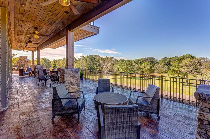 Patio overlooking a lake with seating, wood ceiling and deck, brick columns, and a blue sky.
