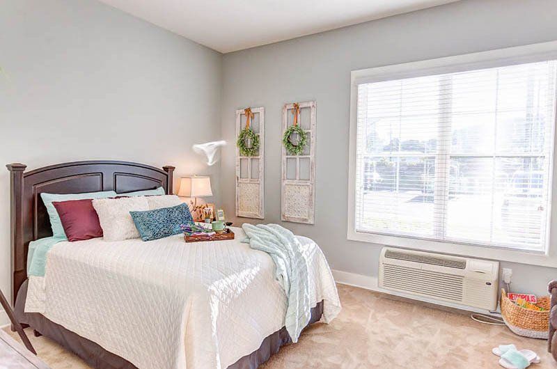 Bedroom with bed, window, and wall decor. Light blue walls, neutral tones.