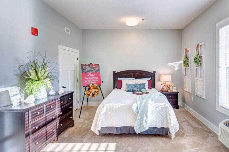 Bedroom with bed, dresser, nightstand, art easel, and neutral-colored walls.