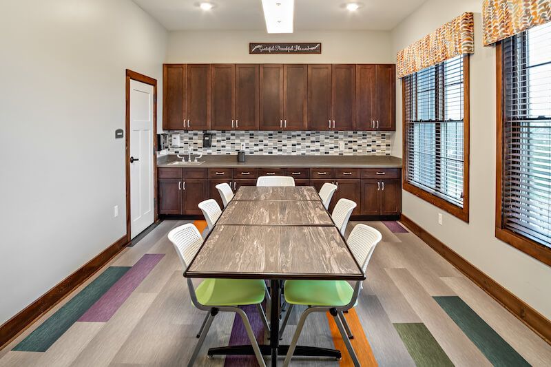 A communal room with a long table, chairs, dark wood cabinets, and colorful floor.