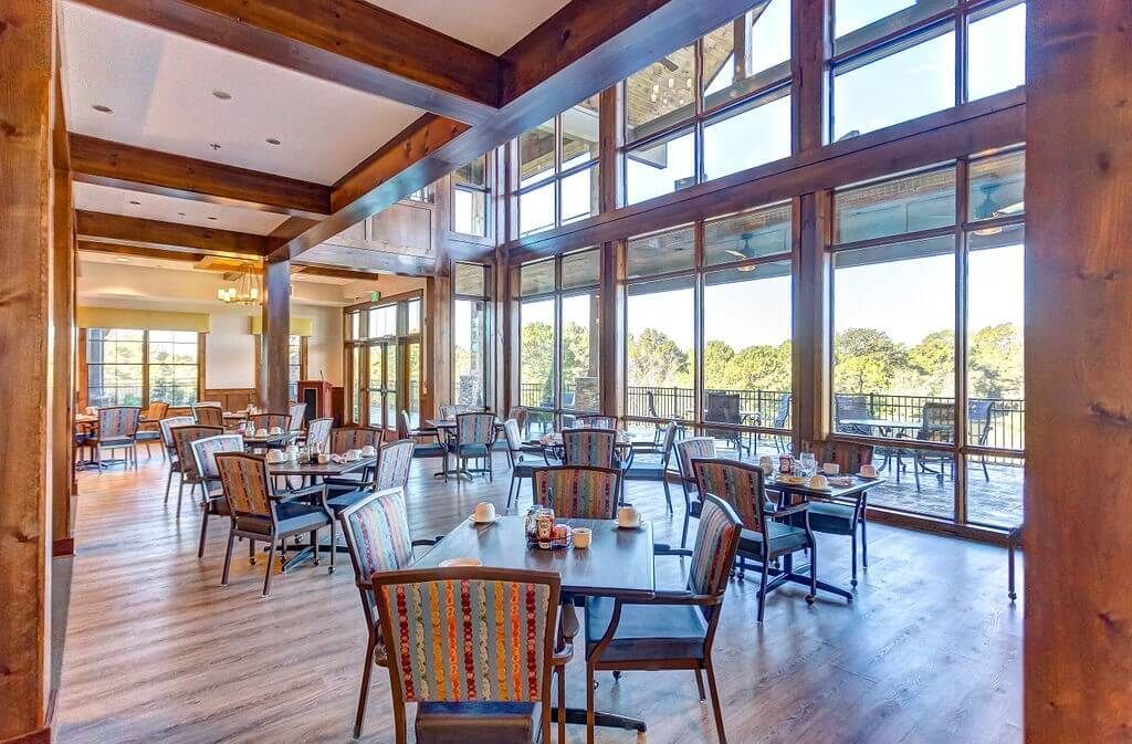 Restaurant dining area with tables, chairs, and large windows overlooking a green outdoor view.