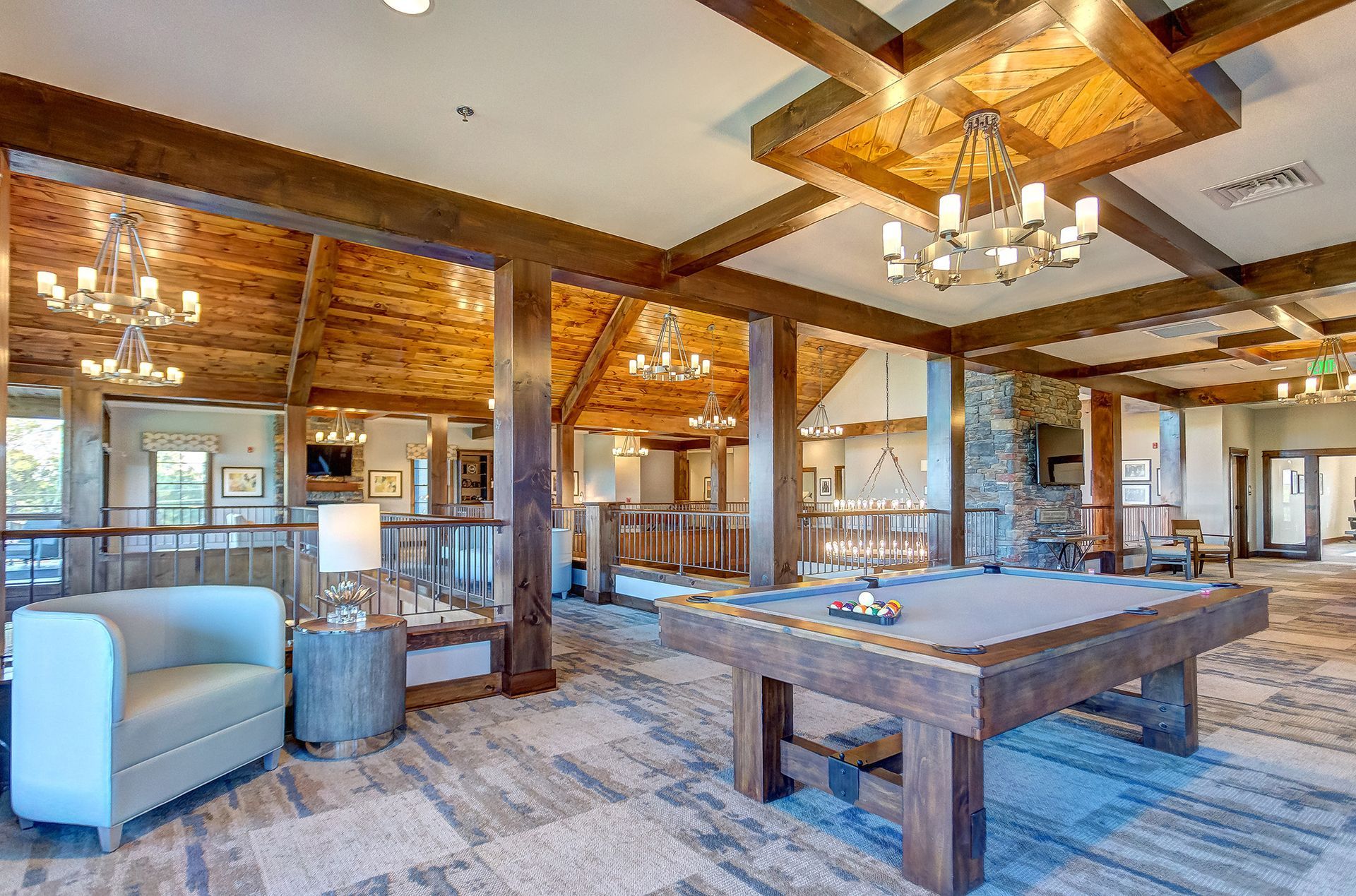 Rustic game room with pool table, seating, exposed beams, and chandeliers.