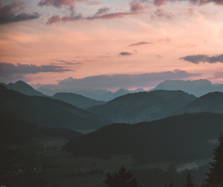 Mountains silhouetted against a pastel sunset sky; pink and orange hues.
