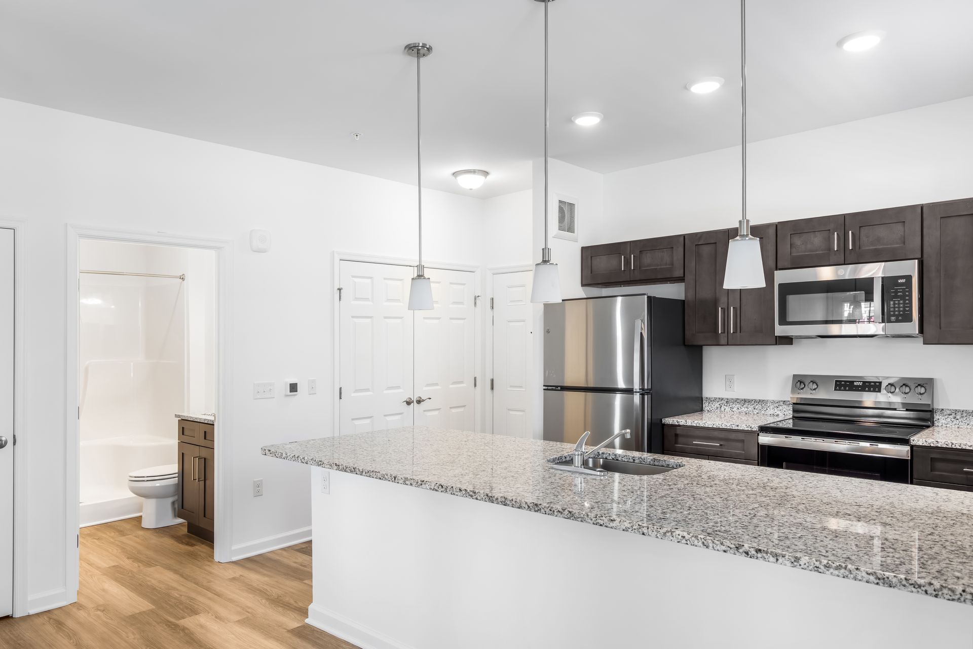 Kitchen with island, stainless steel appliances, dark cabinets, and light granite countertop.