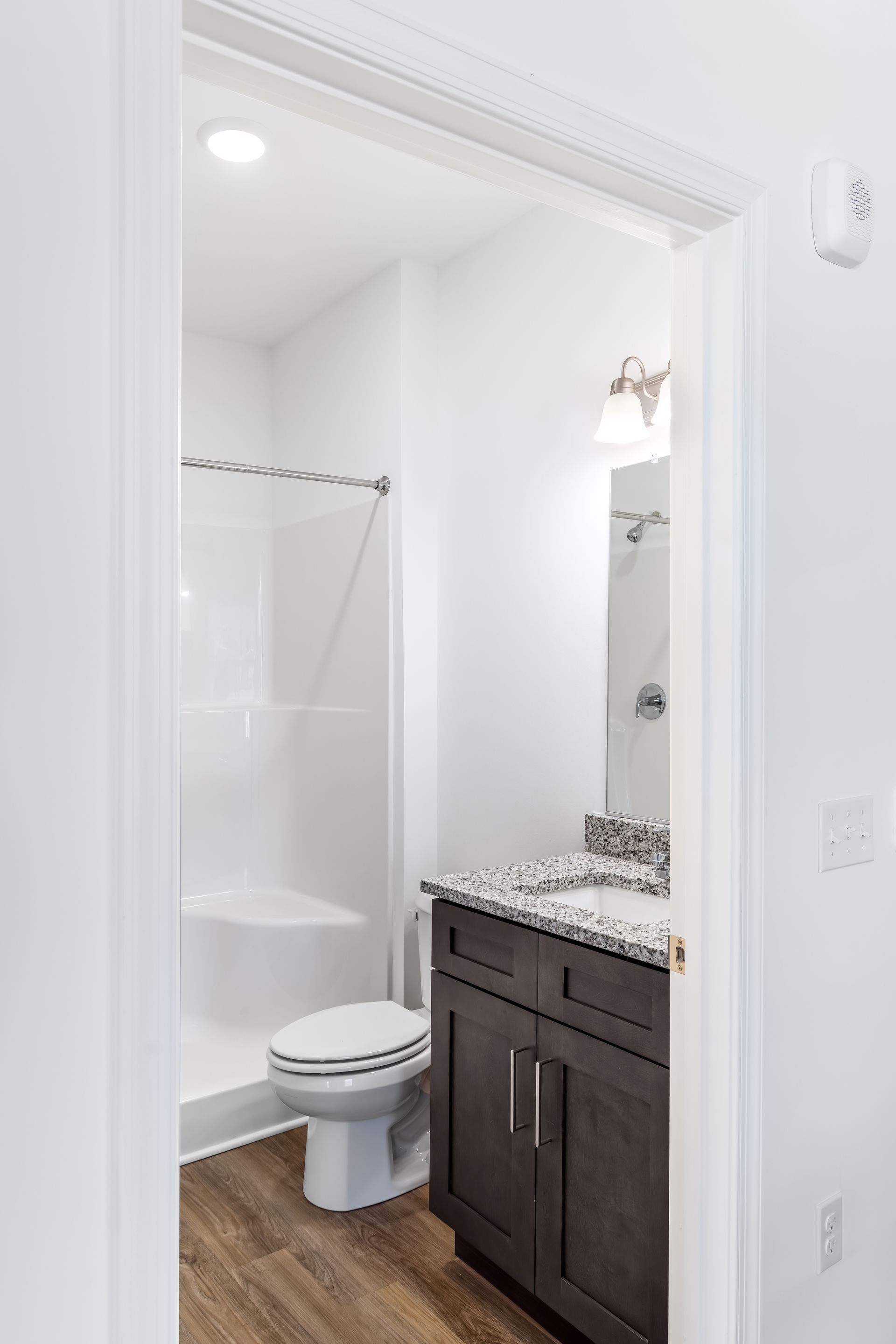 Bathroom with white walls, shower, toilet, dark cabinet, and wood-look flooring.