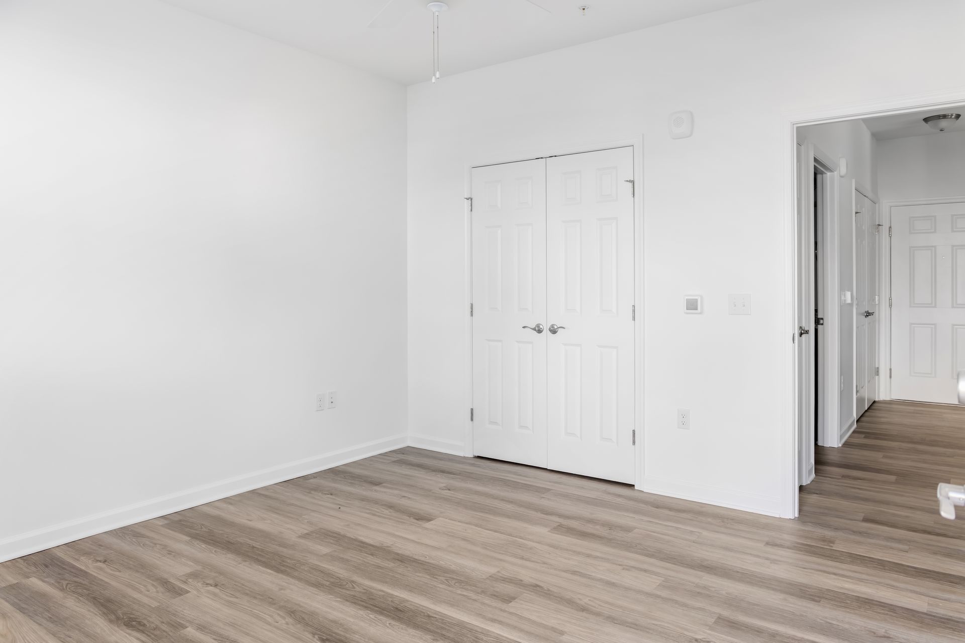 Empty room with white walls, wooden floor, and closet doors.