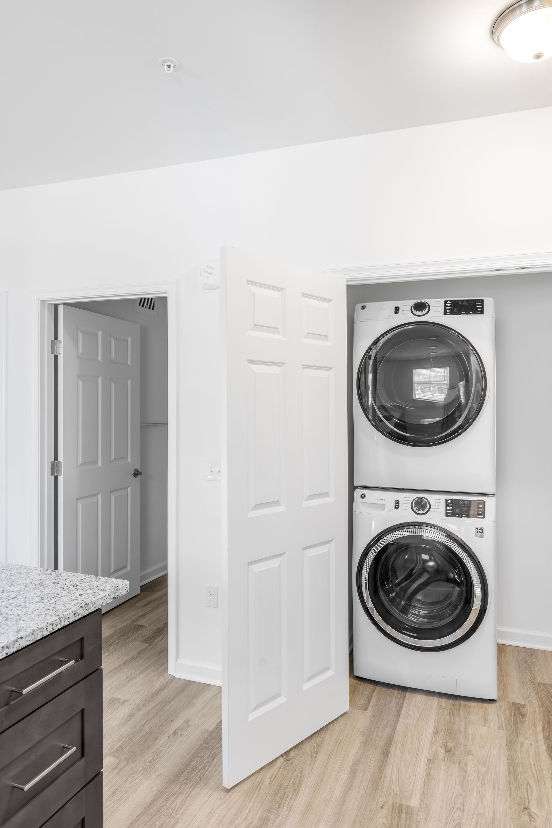 Stacked washer and dryer in a white closet, next to a partially open white door.