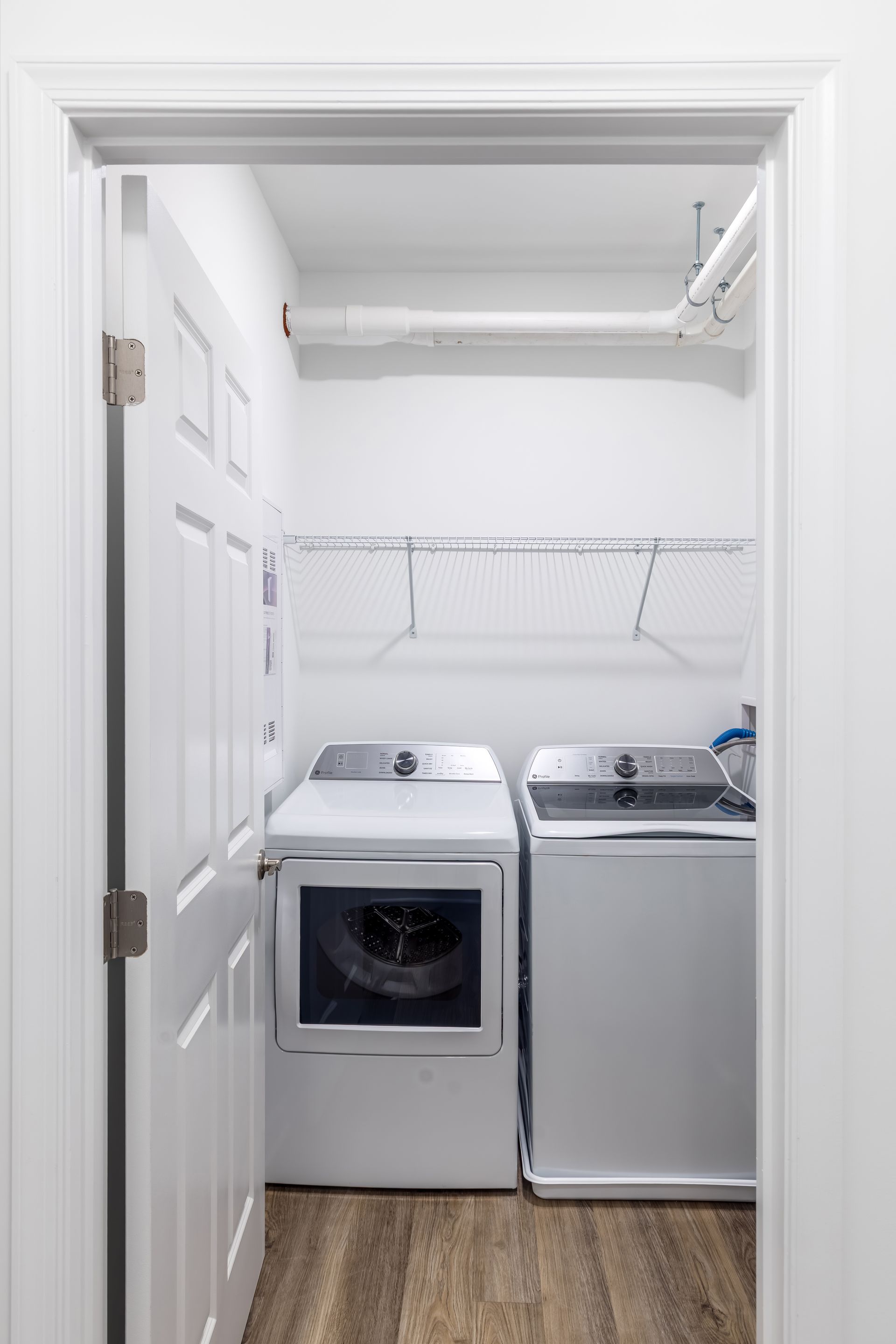 Laundry room with white washer and dryer, open door, and shelving.