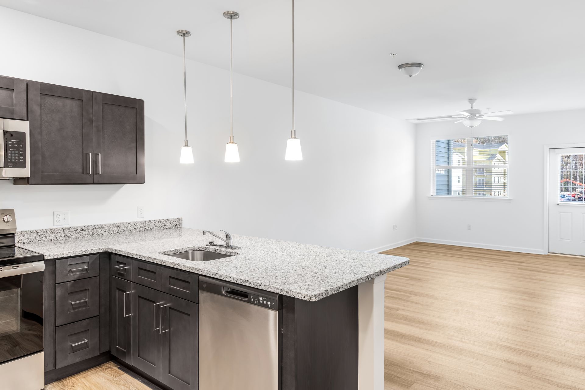 Modern kitchen with dark cabinets, granite counters, stainless steel appliances, and pendant lights over a peninsula.