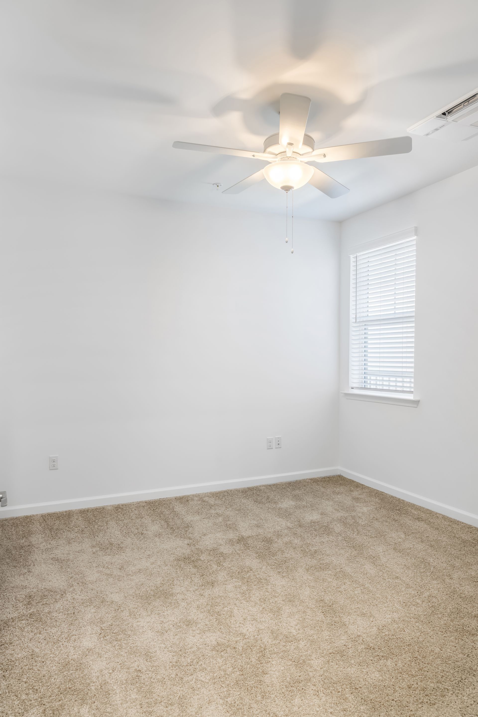 Empty room with beige carpet, white walls, ceiling fan, and window with blinds.