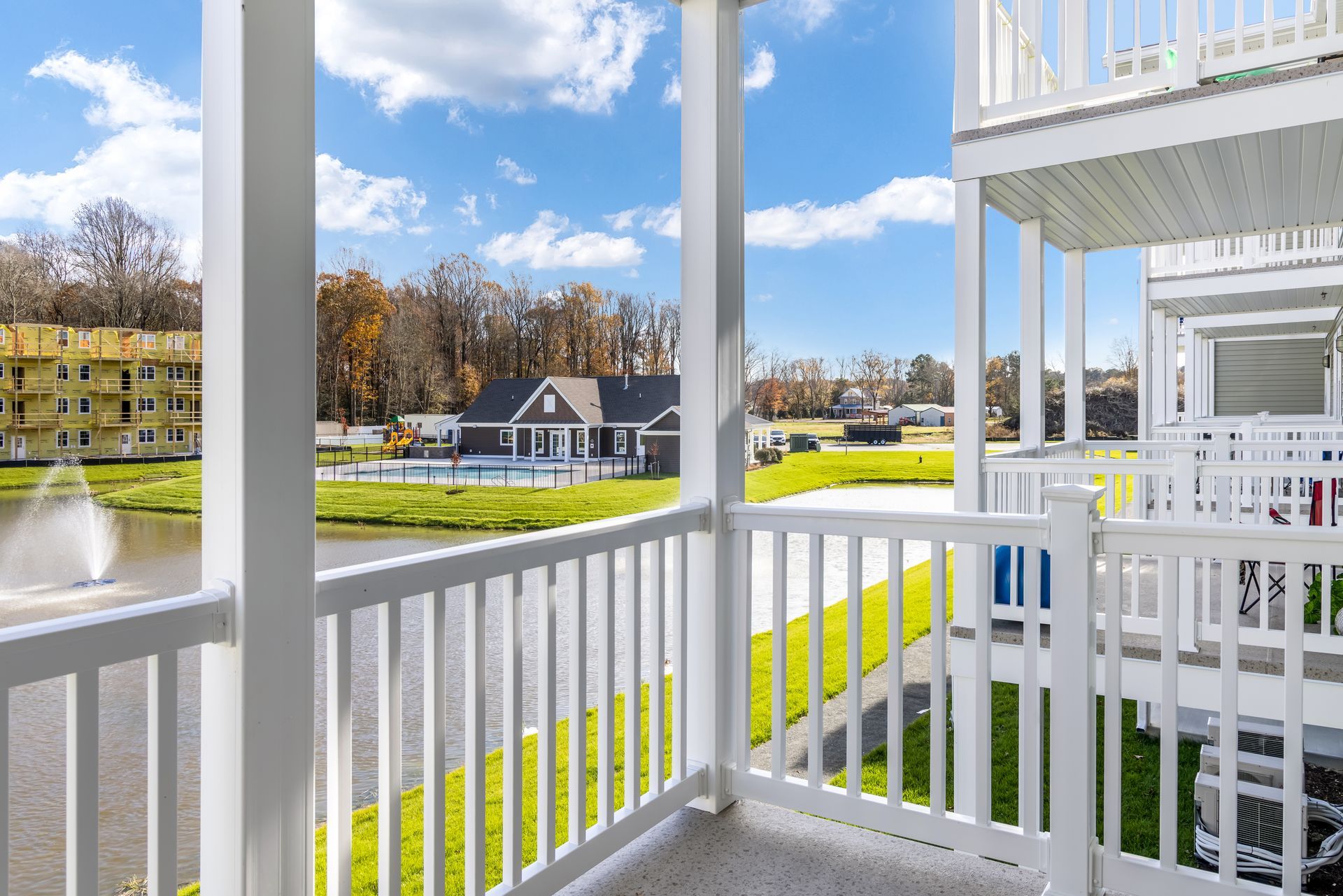 Balcony view overlooking a lake with fountain and a house under a blue sky.