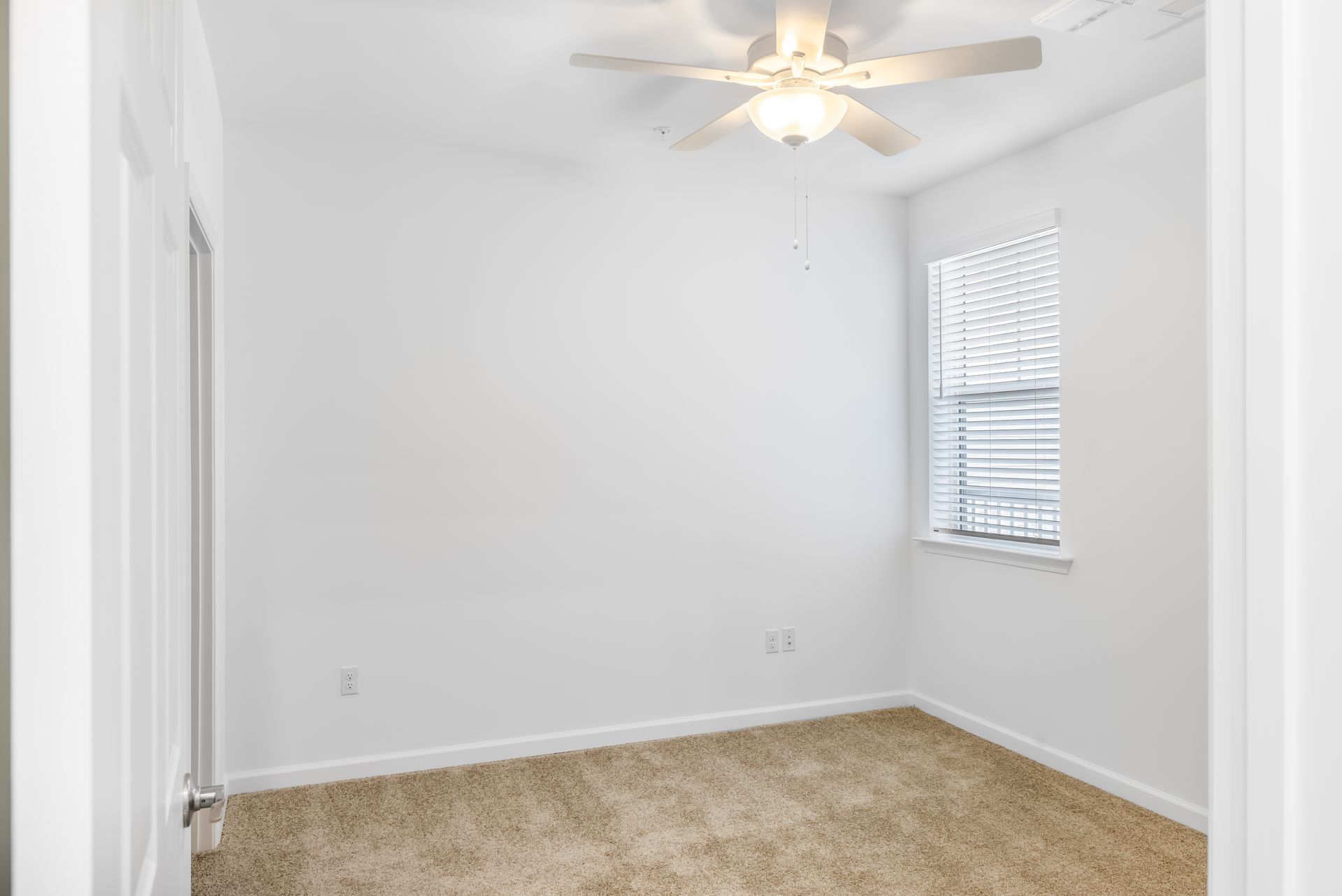 Empty white room with beige carpet, a window, and a ceiling fan.