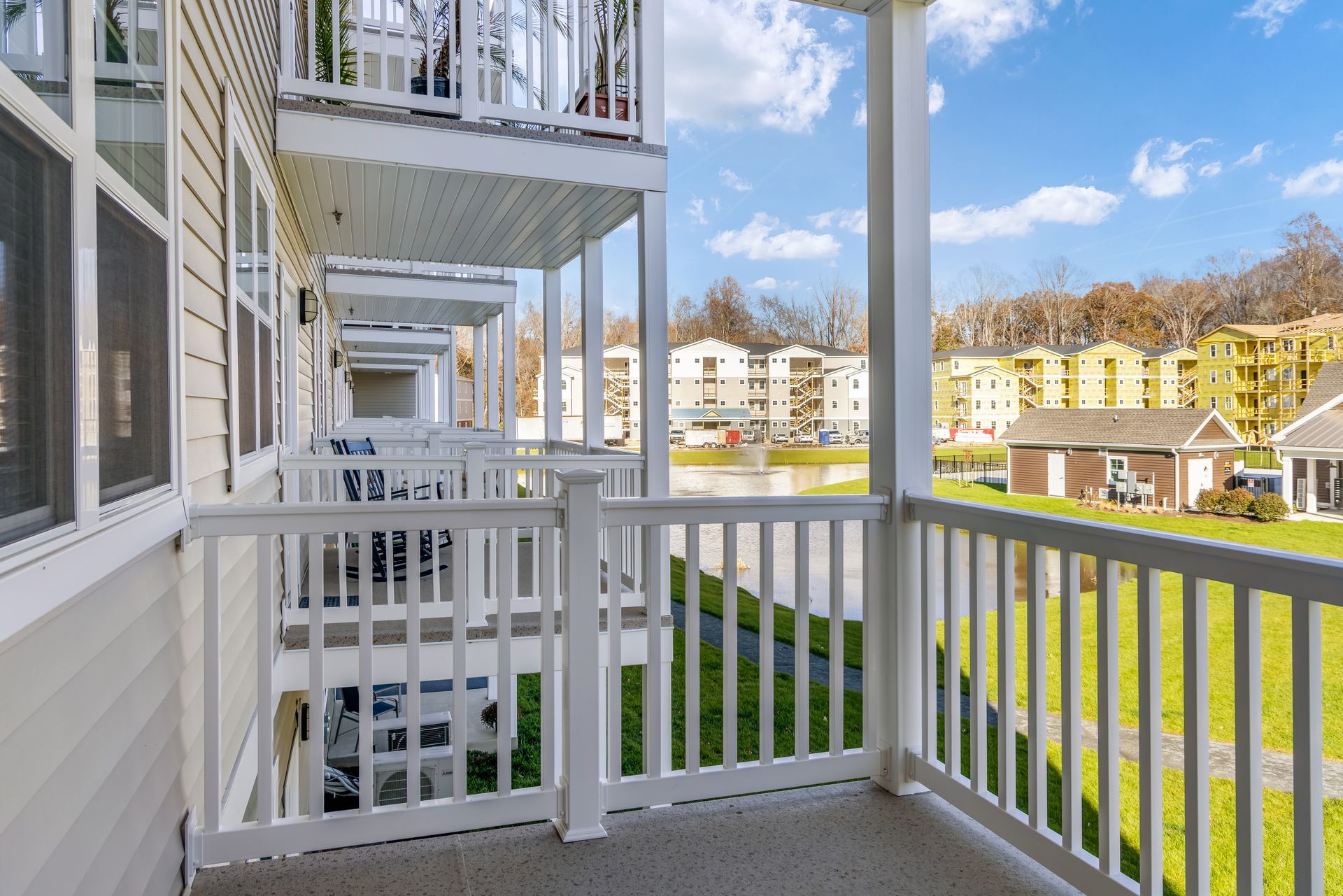 Balcony view of apartments overlooking a green lawn and lake, sunny day.