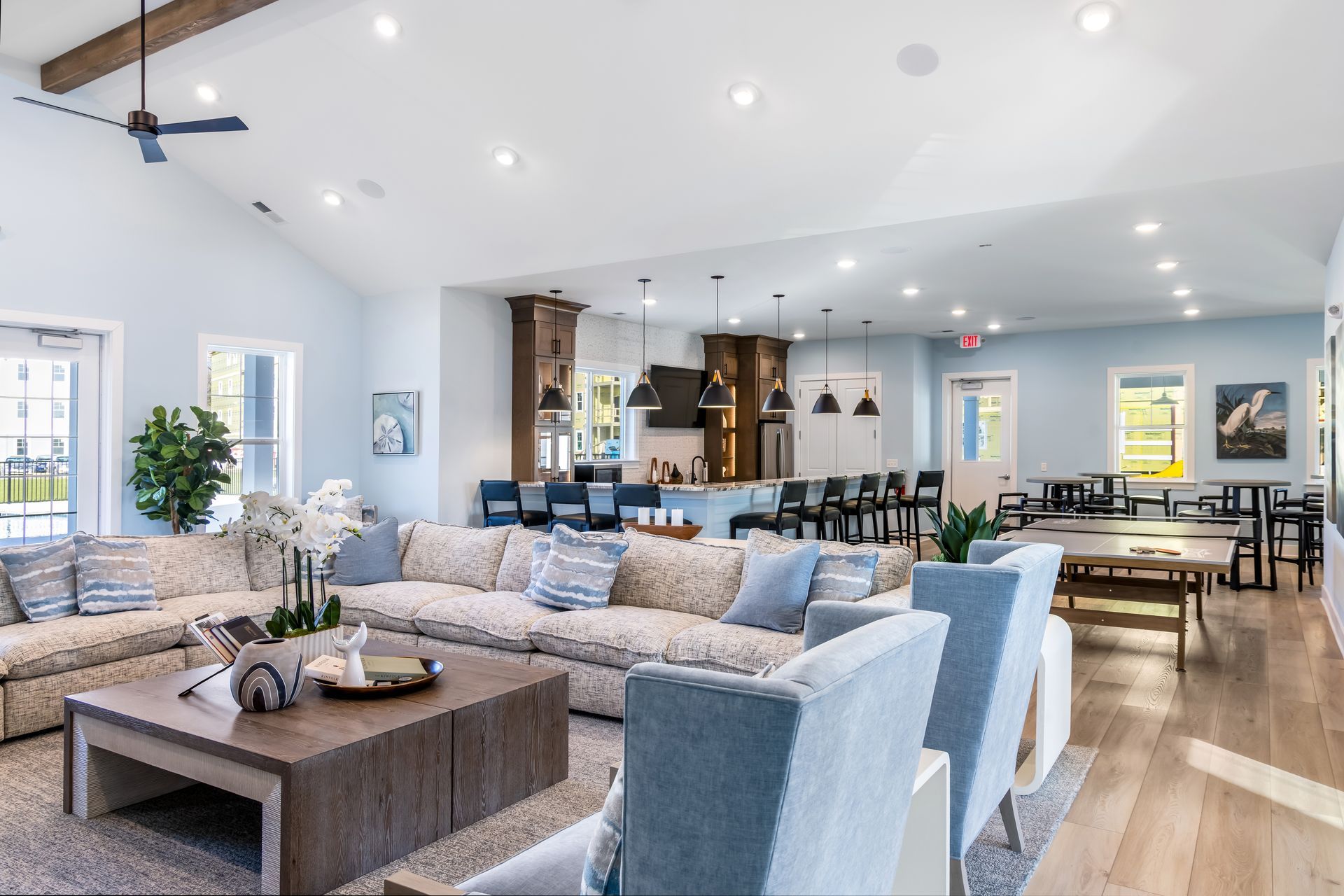 Spacious, light-filled lounge with couches, kitchen area, and a billiards table. Blue and neutral colors.