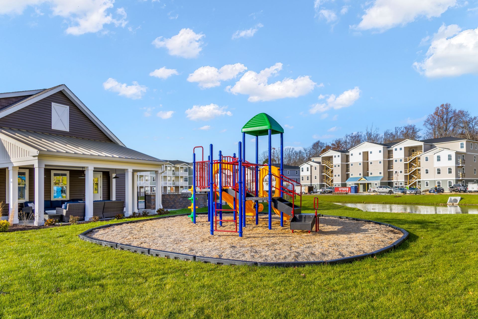 Playground with slide, sand pit, and covered seating area, in front of apartments.