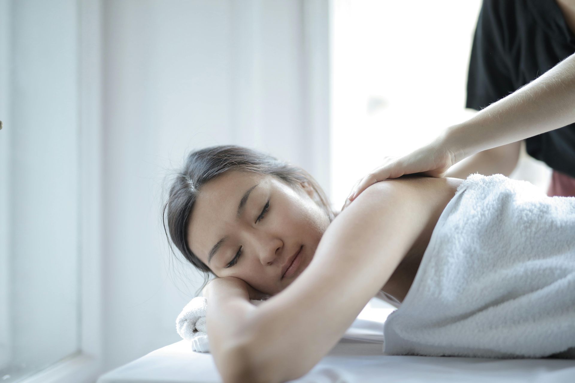 Woman receiving shoulder massage, eyes closed, white towel on spa bed.