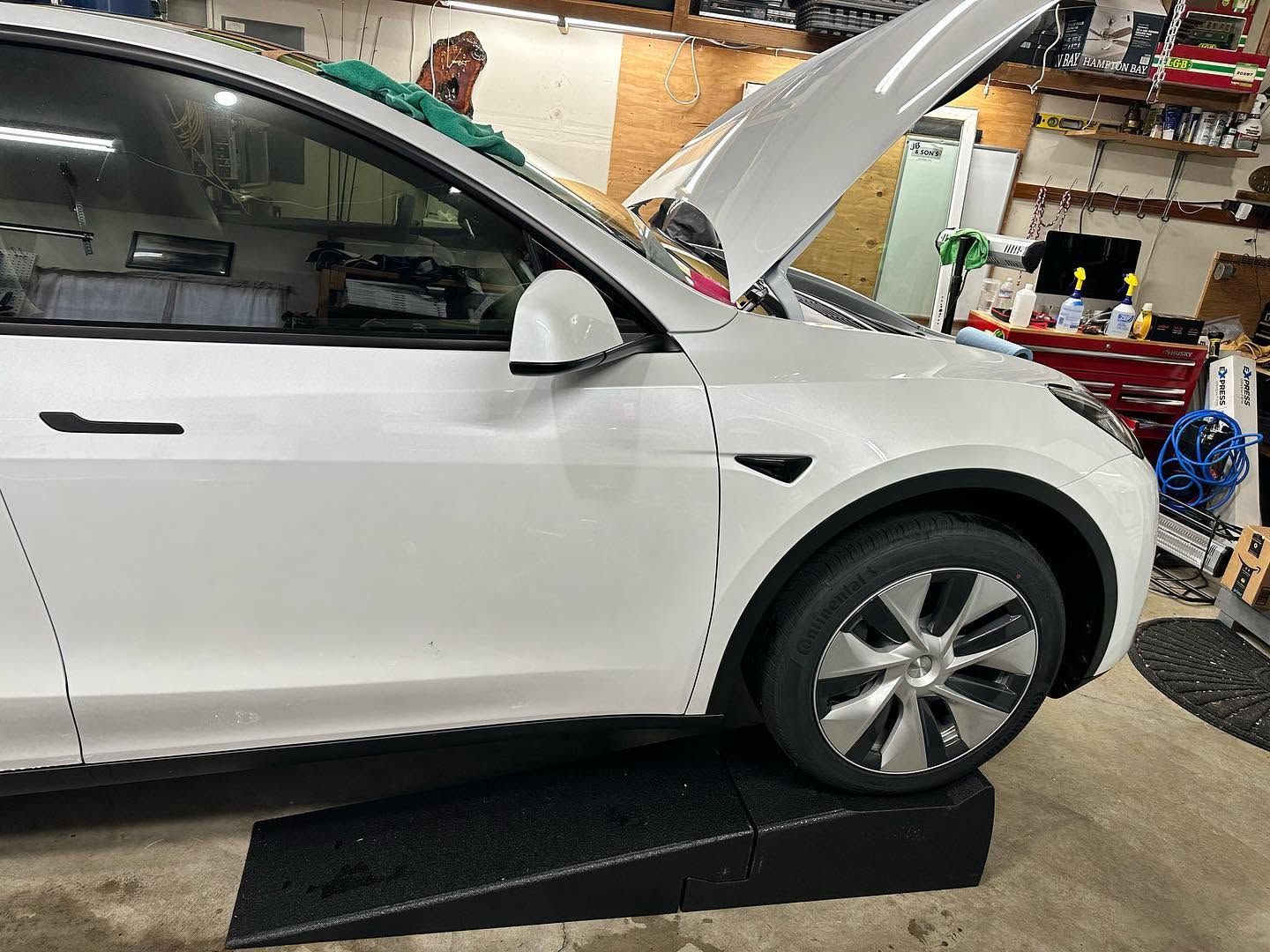 White SUV in a garage with its hood open, parked on a ramp near service equipment.