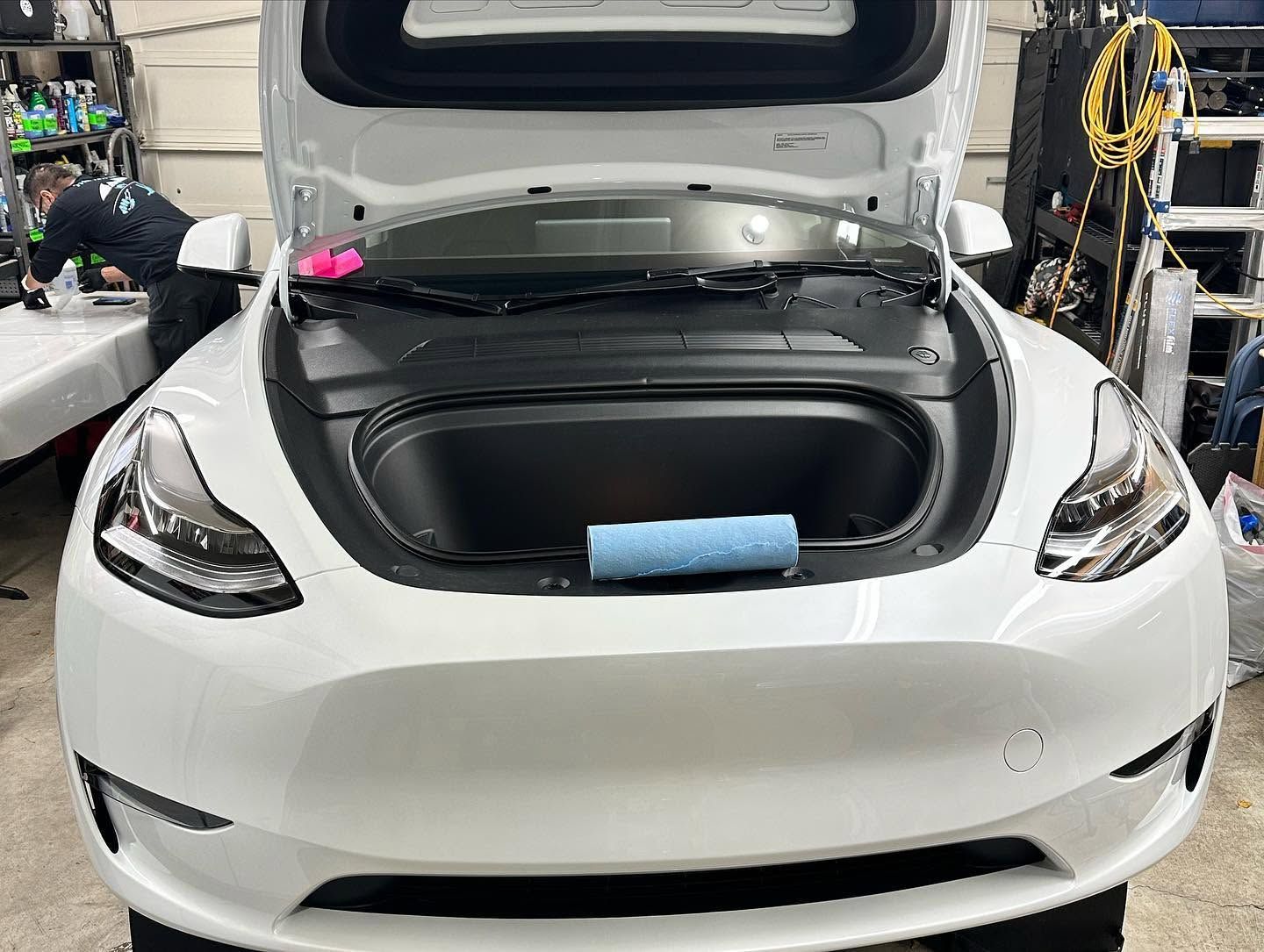 White car with open front trunk in a workshop, showing a blue item inside